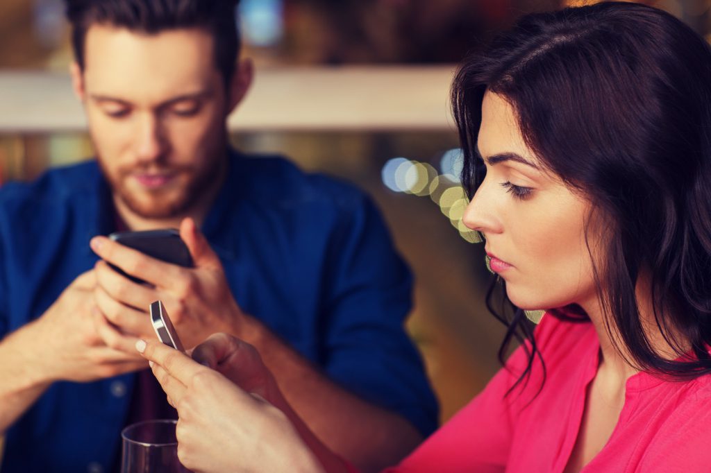 couple with smartphones dining at restaurant