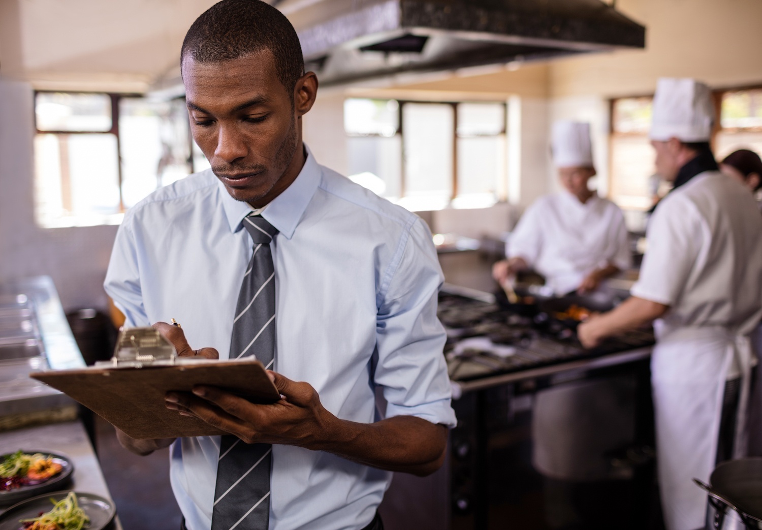 Male manager writing on a clipbaord in kitchen at hotel